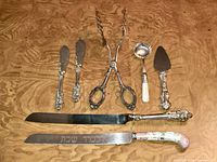 Full view of all nine pieces arranged on wood surface, showing variety of serving utensils including knives, tongs, ladle, and pie server.
