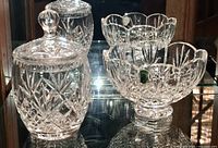 Group photo showing the Waterford crystal covered jar with lid on the left and the footed small bowl on the right, both with intricate cut patterns, on a reflective glass surface.