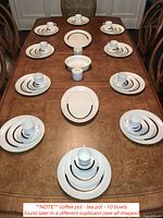 Ten place settings arranged on wood table with stacked plates and cups