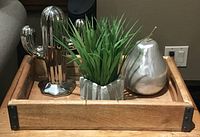 Top view of wooden tray holding three decorative items: chrome cactus figure, faux plant in pot, and silver pear ornament.
