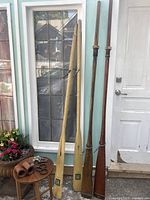 Front view showing four wooden oars arranged side by side, two lighter-colored and taller, two darker and shorter, with leather rowing accessories on a nearby table