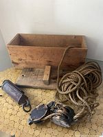 Photo of antique cast iron scale, wooden pulley, rope, and wooden box on table.