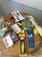 Variety of new fishing lures and tackle in original packaging displayed on round wood table