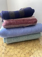 Stack of four folded wool blankets in varying colors and patterns