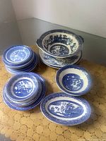 Blue Willow china lot including various plates, bowls and serving bowl laid out on table.