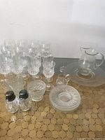 Overview of lot showing the two sets of crystal wine glasses, etched glass plate and jug, salt and pepper shakers, creamers, bowl, and plates on gold circular mat