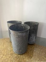 Three vintage metal sap buckets standing upright on a surface, showing their exterior condition.