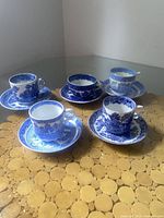 Five assorted vintage Blue Willow pattern tea cups and matching saucers on a surface, each cup and saucer having different design variations in blue and white.