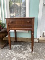 Front view of vintage wooden side table showing drawer and turned legs.