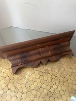 Wooden vintage wall shelf placed on patterned floor showing overall wear and shape.