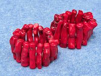 Two chunky red coral branch bracelets laid side-by-side on blue fabric, showing the irregular natural shapes and vibrant red color of the coral pieces.