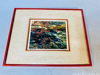 Framed print featuring a red frame and matting showing artwork with red maple leaves over a river scene.