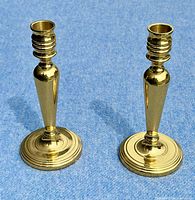 Pair of shiny brass candlesticks shown standing on blue surface, viewed from above, showing top and base details.