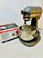 Full view of mixer with stainless steel bowl, wire whip and boxed KitchenAid slicer and shredder accessory