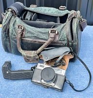 Camera bag open showing Minolta Super 3 Circuit camera, detachable grip, leather case, strap, and additional accessories