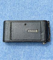 Closed view of the camera showing the textured black leather exterior and Kodak branding plate on the front panel.