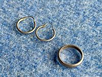 Plain sterling silver small hoop earrings and a plain sterling silver band ring displayed on blue fabric.