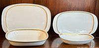 Two pairs of fine bone china trays and bowls, white with gold trim, shown side by side on a wooden surface.