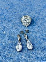 Pair of large clear cubic zirconia teardrop dangle earrings on a blue textured background.