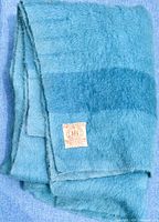 Folded blue wool Hudson's Bay point blanket with visible label showing brand and material info against a blue textured surface.