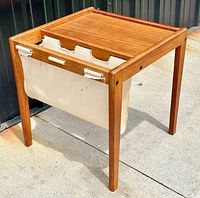 Side angle showing teak table with canvas sling for magazines