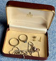 Open Birks box showing two sterling silver rings, a silver chain necklace with pink Swarovski pendant, and gold-filled stud earrings on cream felt lining.