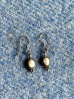 Pair of vintage sterling silver and freshwater pearl earrings on blue textured cloth showing full front view.