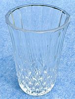 Clear heavy crystal vase standing on a blue background, showing full height and faceted design.