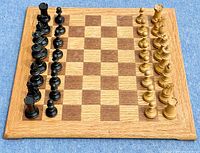 Full view of wooden chessboard with complete set of light and dark wooden chess pieces arranged at starting positions.