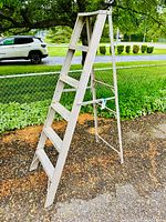 6 foot folding aluminum step ladder in an outdoor setting beside a fence and tree.