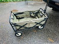 Front and angled view of green fabric collapsible wagon on black metal frame with visible wheels and handle.