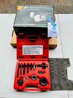 Photo showing top view of the Cleveland Air Spot Sandblaster box on top of a cardboard box with the red plastic case for the pulley puller set below it, with tools neatly set inside.