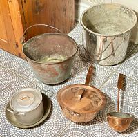 Photo showing the full collection of antique copper and metalware items on tiled floor, including cauldron, pots, ladles, and bucket.