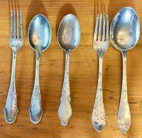 Three antique silver flatware pieces laid out on wood surface showing two forks and one spoon with hammered handle patterns.