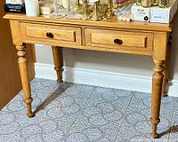 Full view of antique maple wood console table with two drawers and round dark knobs, showing turned legs and light wood finish.