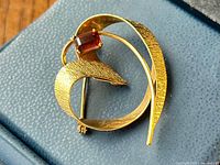 Close-up view of brooch on grey surface showing textured gold curves and citrine stone