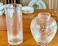 Tall clear cylindrical glass vase standing upright on wood surface.