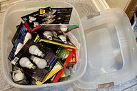 Large plastic bin filled with multiple light bulbs in original packaging and some loose bulbs.