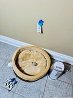 Photo of circular heated pet bed adjacent to white Bionaire air cleaner tower with attached electrical cord.