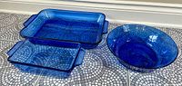 Two blue rectangular glass casseroles and one blue round glass bowl arranged on tiled floor.