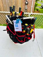 White bucket with black and red fabric tool holster full of various screwdrivers and tools standing on a table.