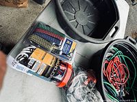 Photo of assorted bungee cords, packaged Maxload cords, flat woven straps, and black plastic containers