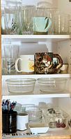 Top shelf with assorted clear glass drinking glasses and ceramic mugs with designs