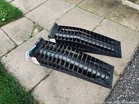 Pair of black plastic car ramps on concrete ground showing full length and shape.
