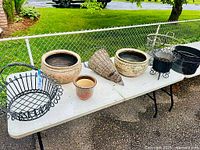 Wide shot of six assorted planters displayed on a folding table outdoors, showing overall lot contents and types of planters included.