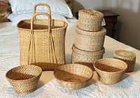 Photo showing full collection of 8 woven baskets in various shapes and sizes laid out on a bed.