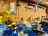 Workbench area showing two bench vises, plastic containers with lids, hand tools, and parts organized on pegboard and workbench.