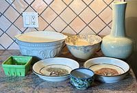 Seven ceramic kitchen items arranged on countertop showing variety of shapes, sizes, and decorative patterns including mixing bowls and vase.