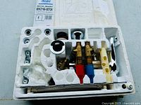 Full look at the repair kit showing foam packaging holding brass and metal components including valves with red and blue handles, connectors, and mounting parts.
