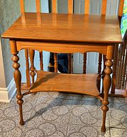 Full view of the antique golden oak wash stand table showing top surface, turned legs, and lower shelf against tile floor.